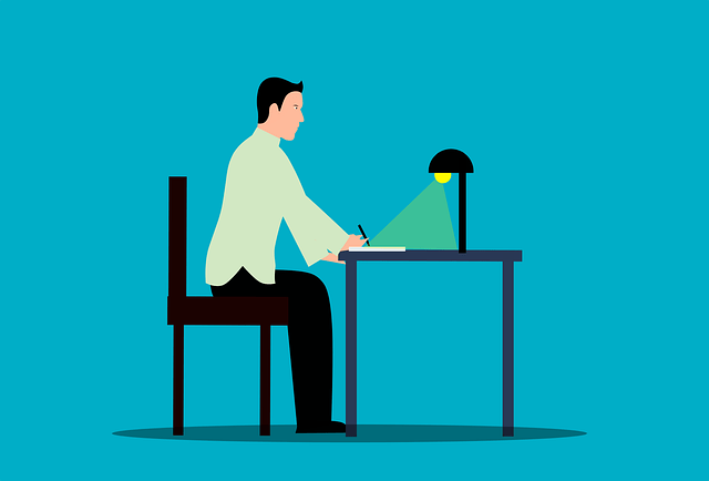 Writer sits at a desk writing with pen in hand beneath a desk lamp
