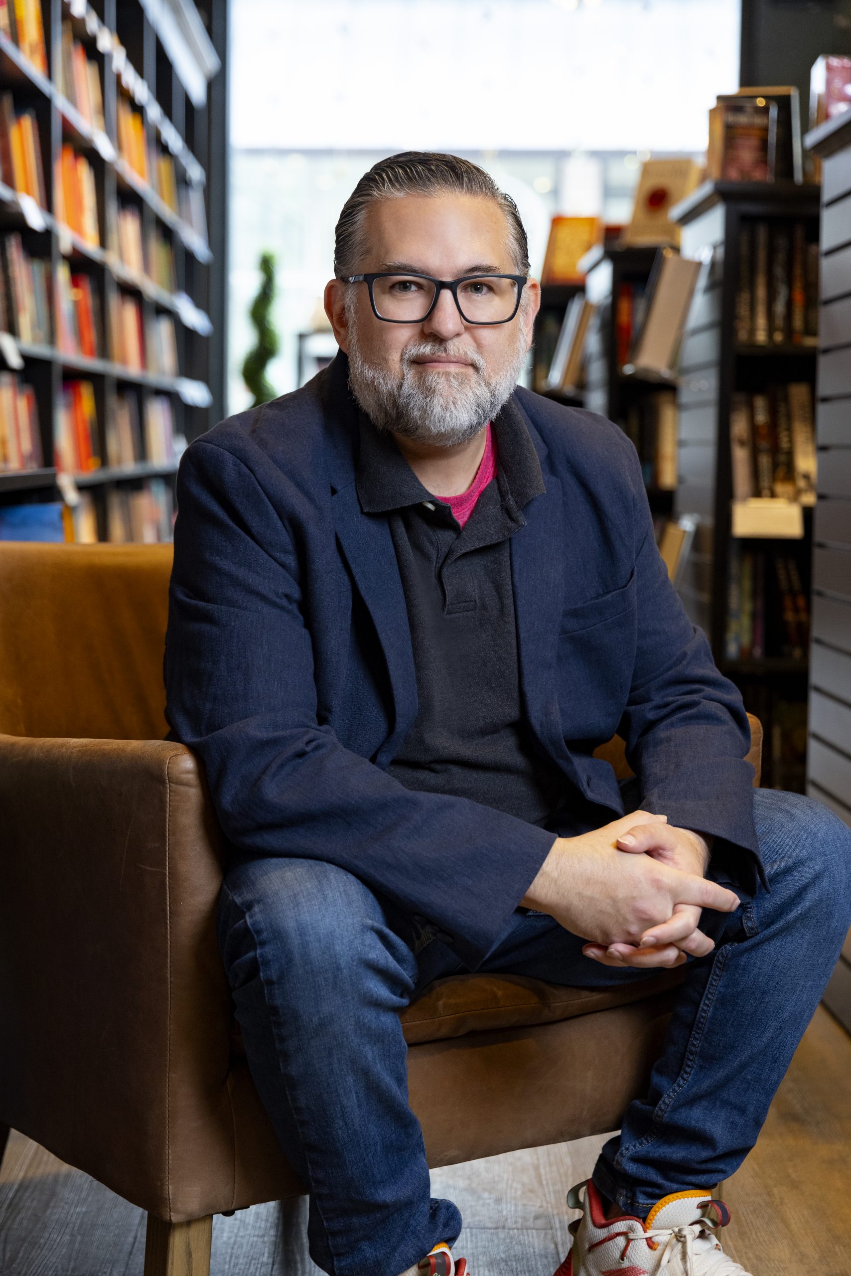 Literary and illustration agent Carter Hasegawa, dark hair, glasses, white beard, seated, wearing navy blue jacket and jeans