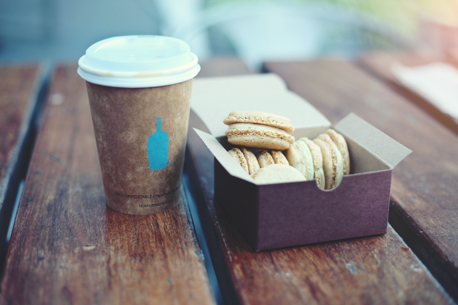 macaroons in a purple box, cofee in a recyclable cup on a wooden table