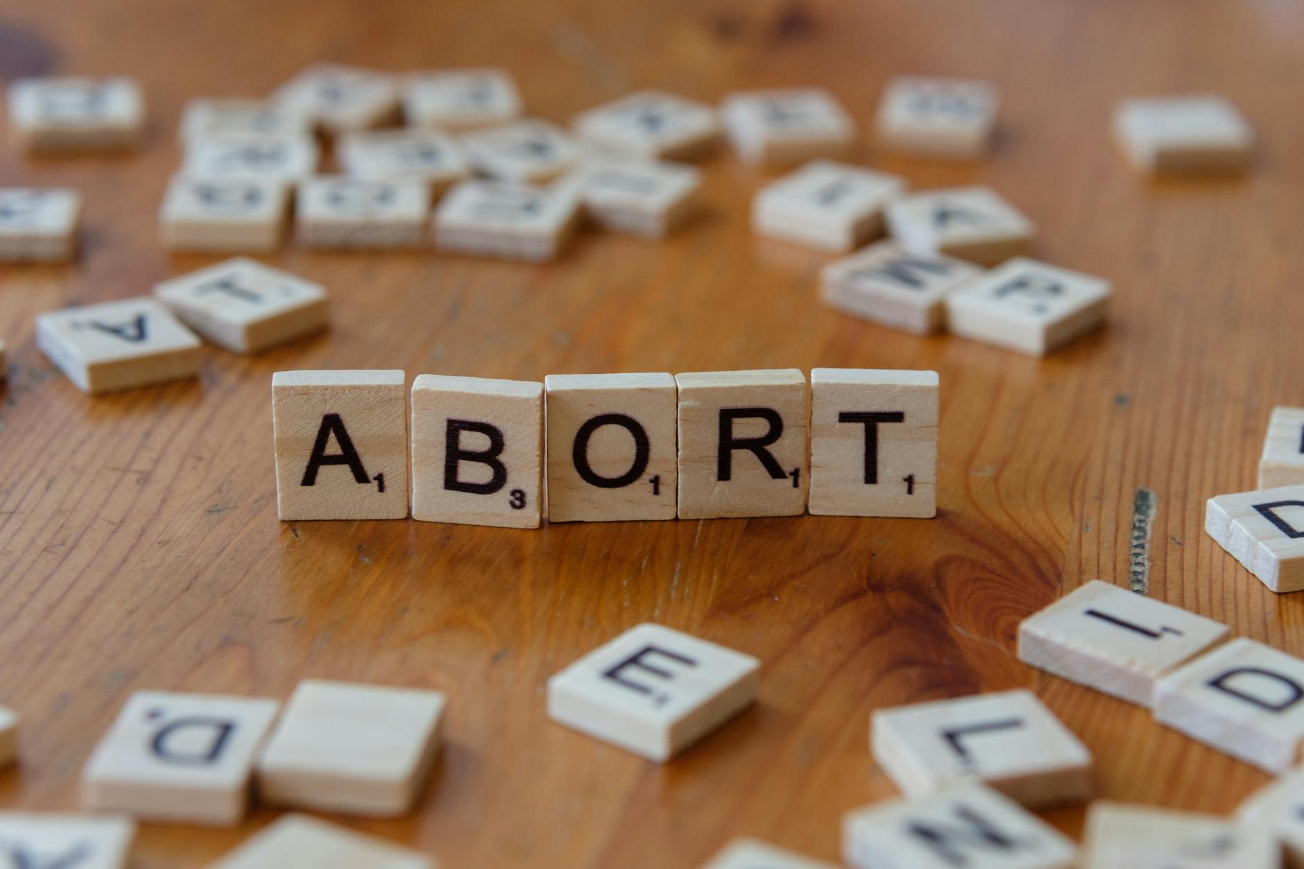 abort word on scrabble tiles on wood surface