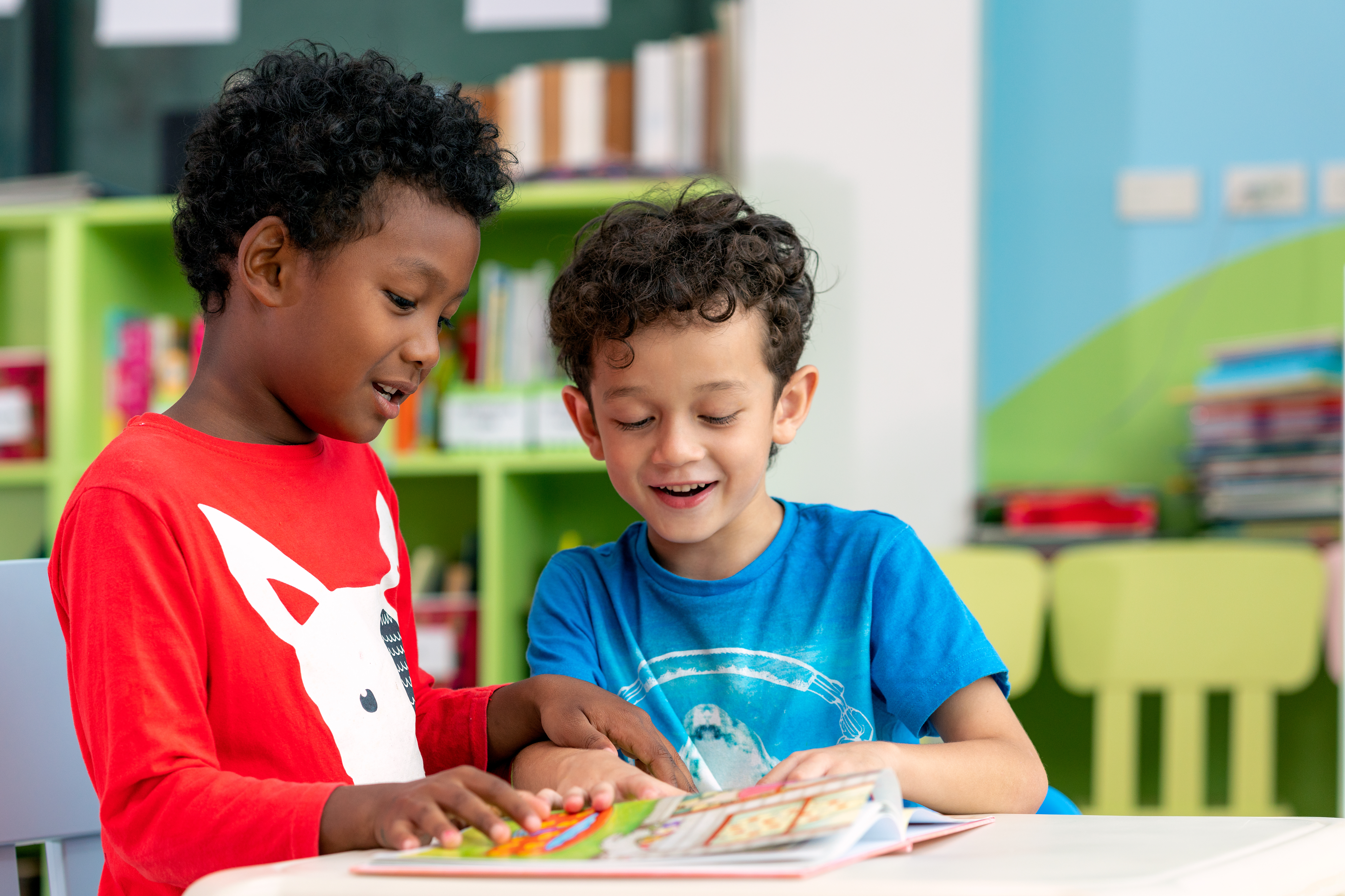 Two young boys in a classroom look at a book together.