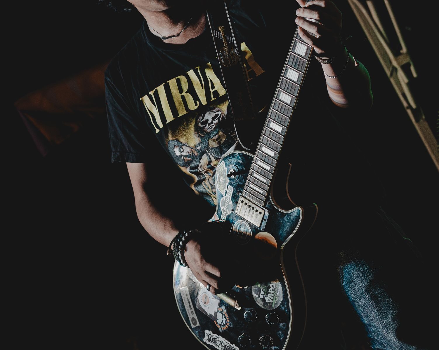 Close-up of a guitarist playing an electric guitar indoors, wearing a Nirvana shirt.