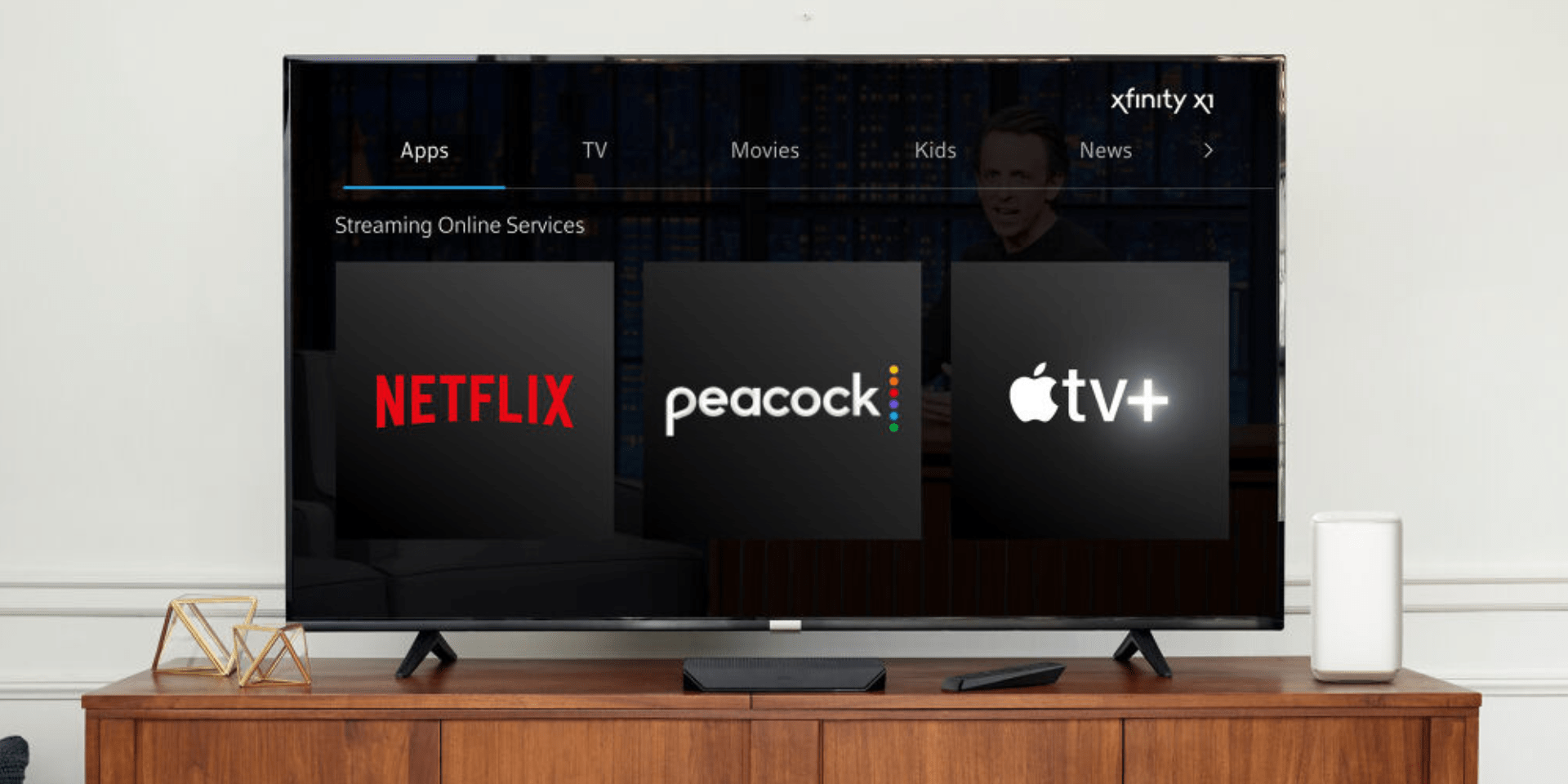 An image of a flat screen TV on top of a wooden entertainment center. The TV screen displays the Xfinity StreamSaver interface. The interface shows four sections: Apps, TV, Movies, and Kids & News. Under the Apps section, there are three icons for streaming services: Netflix, Peacock, and Apple TV+. Text at the top right of the image says "xfinity xi".