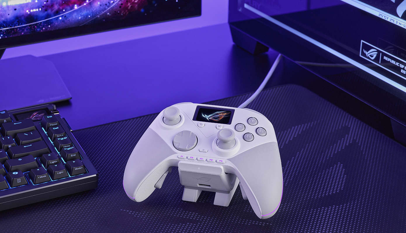 ASUS ROG Raikiri II Pro PC controller placed on a gaming desk between a mechanical keyboard and dual monitors with purple RGB lighting. The controller features a built-in display, programmable buttons, and a charging dock, highlighting its premium gaming setup.