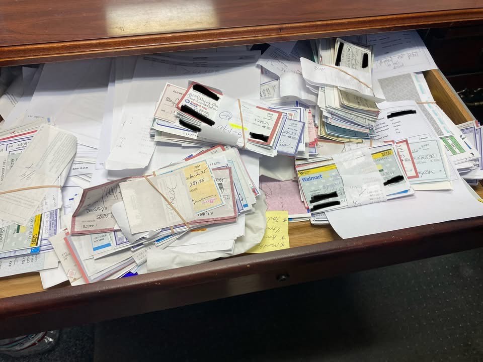 Open desk drawer filled with stacks of bundled checks and paperwork organized with rubber bands.