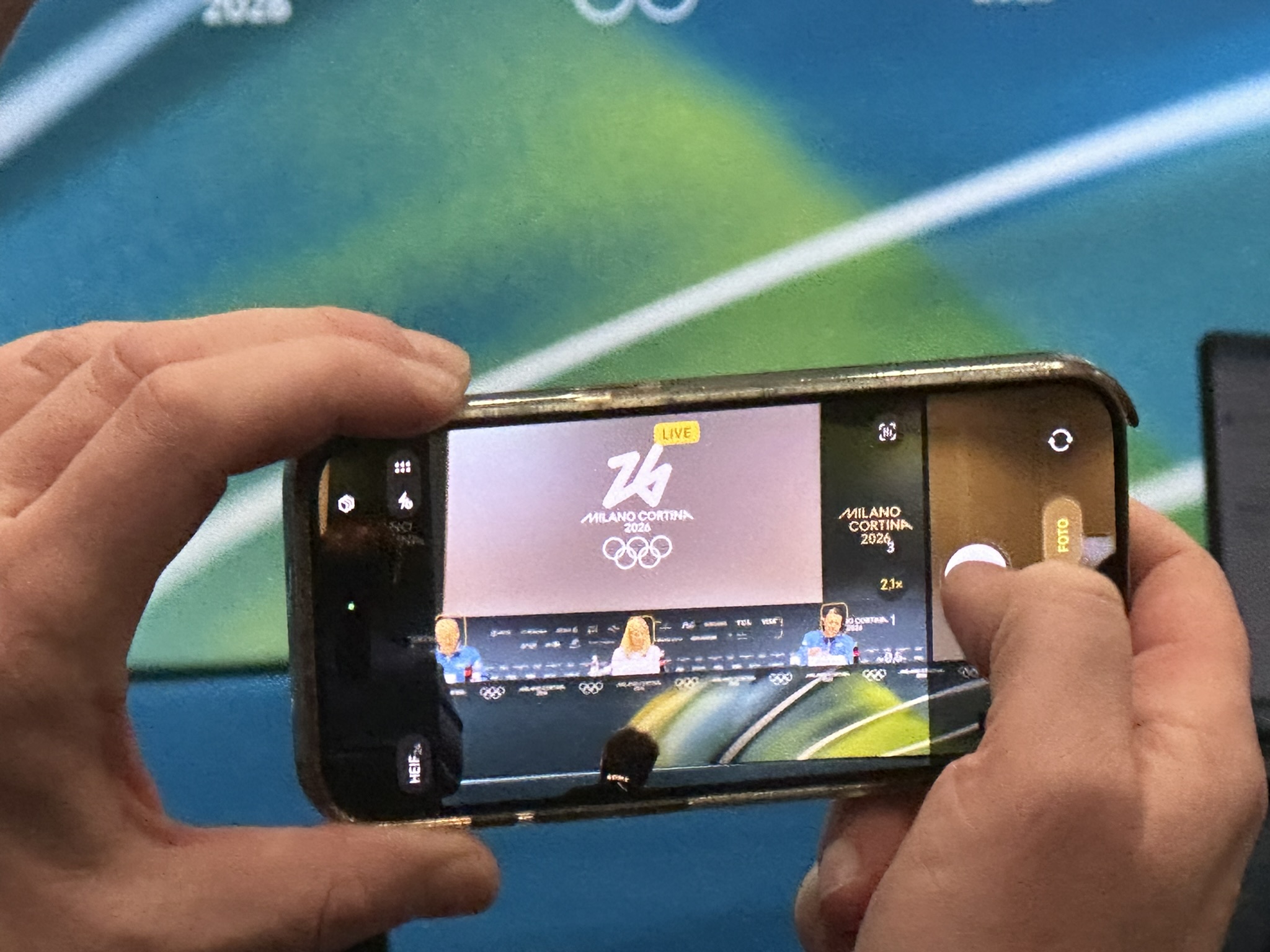 Journalist framing shot of (left to right) IOC Director of Communications Mark Adams, IOC President Kirsty Coventry and IOC Executive Director Christophe Dubi at press conference in the Main Press Center of the Milan Cortina Olympic Winter Games February 13, 2026 (GamesBids photo)