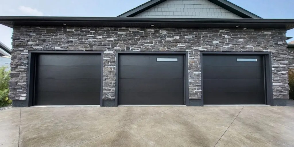 Modern garage door installation featuring three sleek black doors with horizontal panels, set against a stone exterior, showcasing stylish and energy-efficient design for homes in London, Ontario.