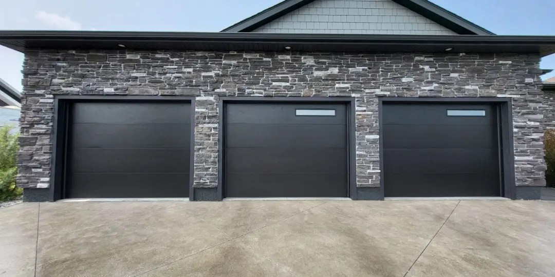 Modern garage door installation featuring three sleek black doors with horizontal panels, set against a stone exterior, showcasing stylish and energy-efficient design for homes in London, Ontario.