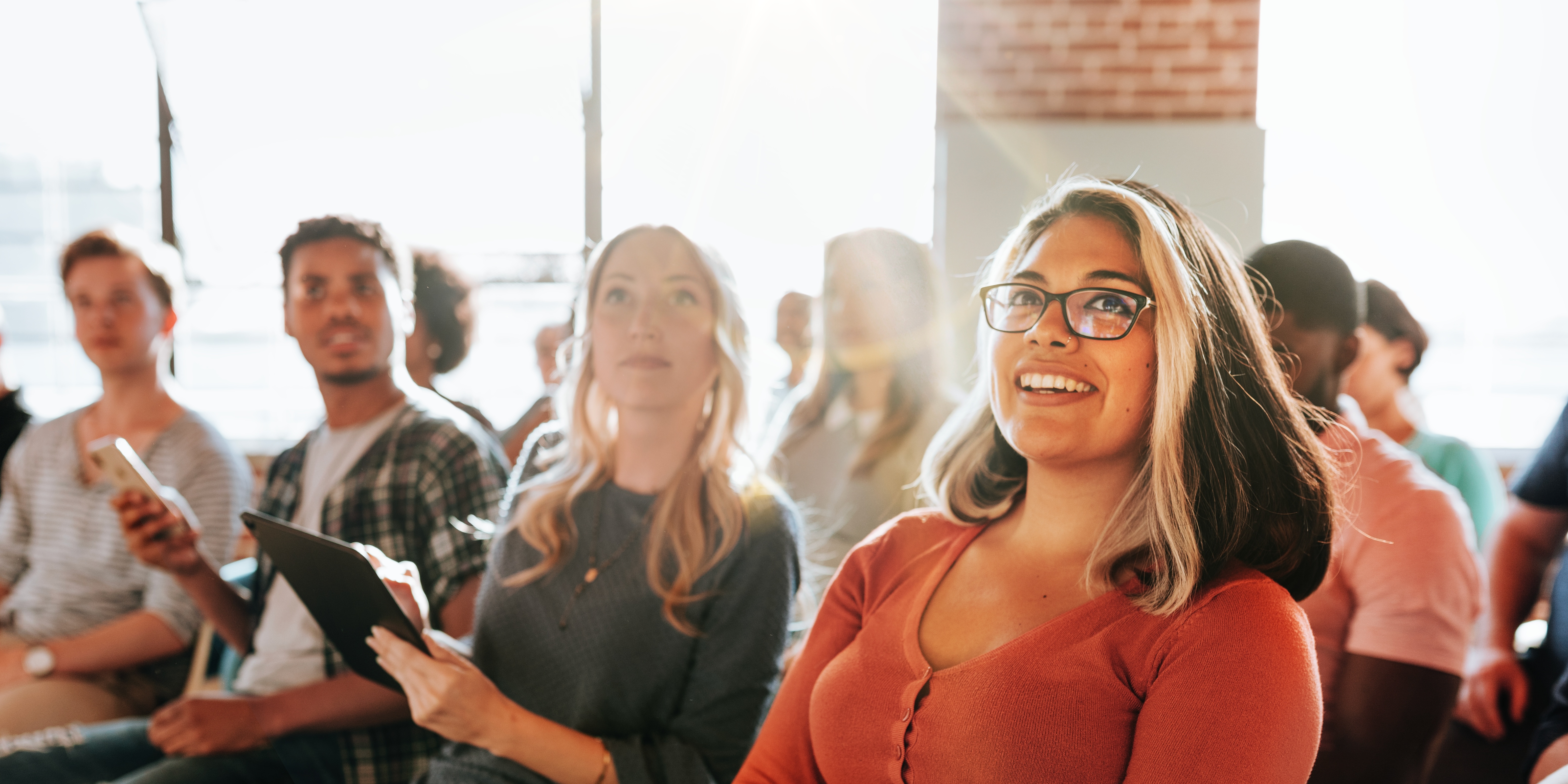 Diverse group of people, including a smiling woman, attending seminar. The seminar audience includes men and women of various ethnicities, all engaged in the seminar. Community seminar with audience.
