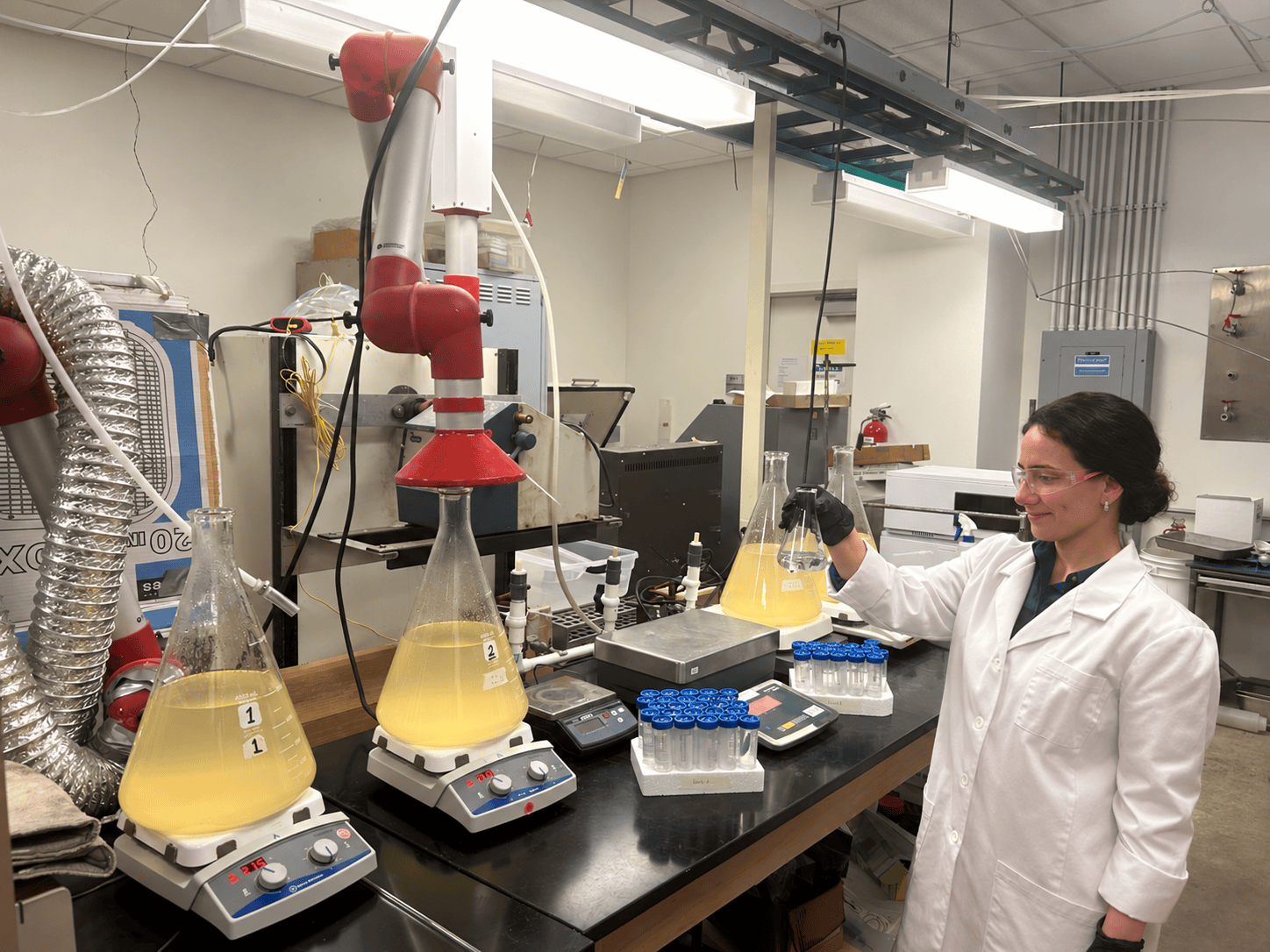 Flasks of yellow brine solution on stirring hot plates in the lab, with a researcher holding a flask of clear liquid.