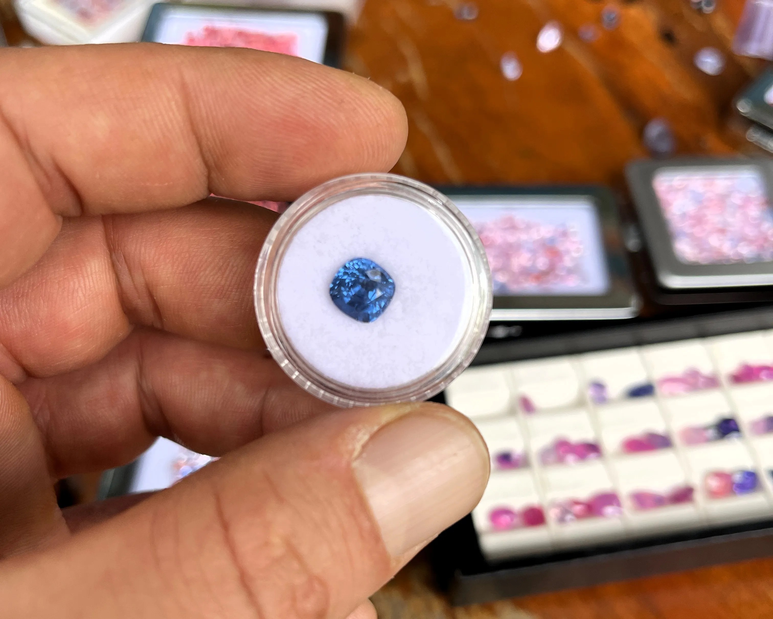 Ein blauer Farbedelstein auf weisser Präsentierschale wird zwischen Daumen und Zeigefinger gehalten