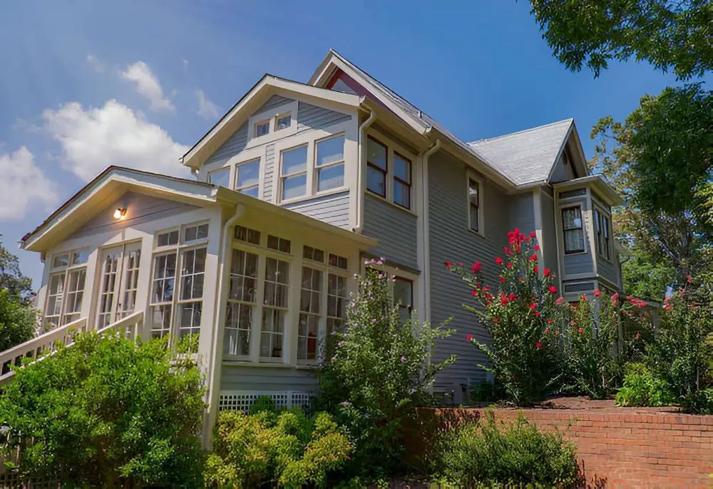 Classic house with sunroom addition and garden landscaping on a sunny day.