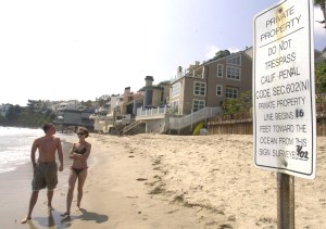 FILE - This Aug. 3, 2002, file photo shows people walking past a sign stating that this beach, in Malibu, Calif., is private property. A Superior Court judge upheld an action by the California Coastal Commission on Tuesday, July 12, 2011, to provide public access to Carbon Beach in Malibu. Judge James C. Chalfant upheld a Commission-issued cease and desist order, which directed Lisette Ackerberg and the Lisette Ackerberg Trust to allow opening up of the public entry from the Pacific Coast Highway to the beach, and to remove a number of items blocking the entry. (AP Photo/Reed Saxon, File)