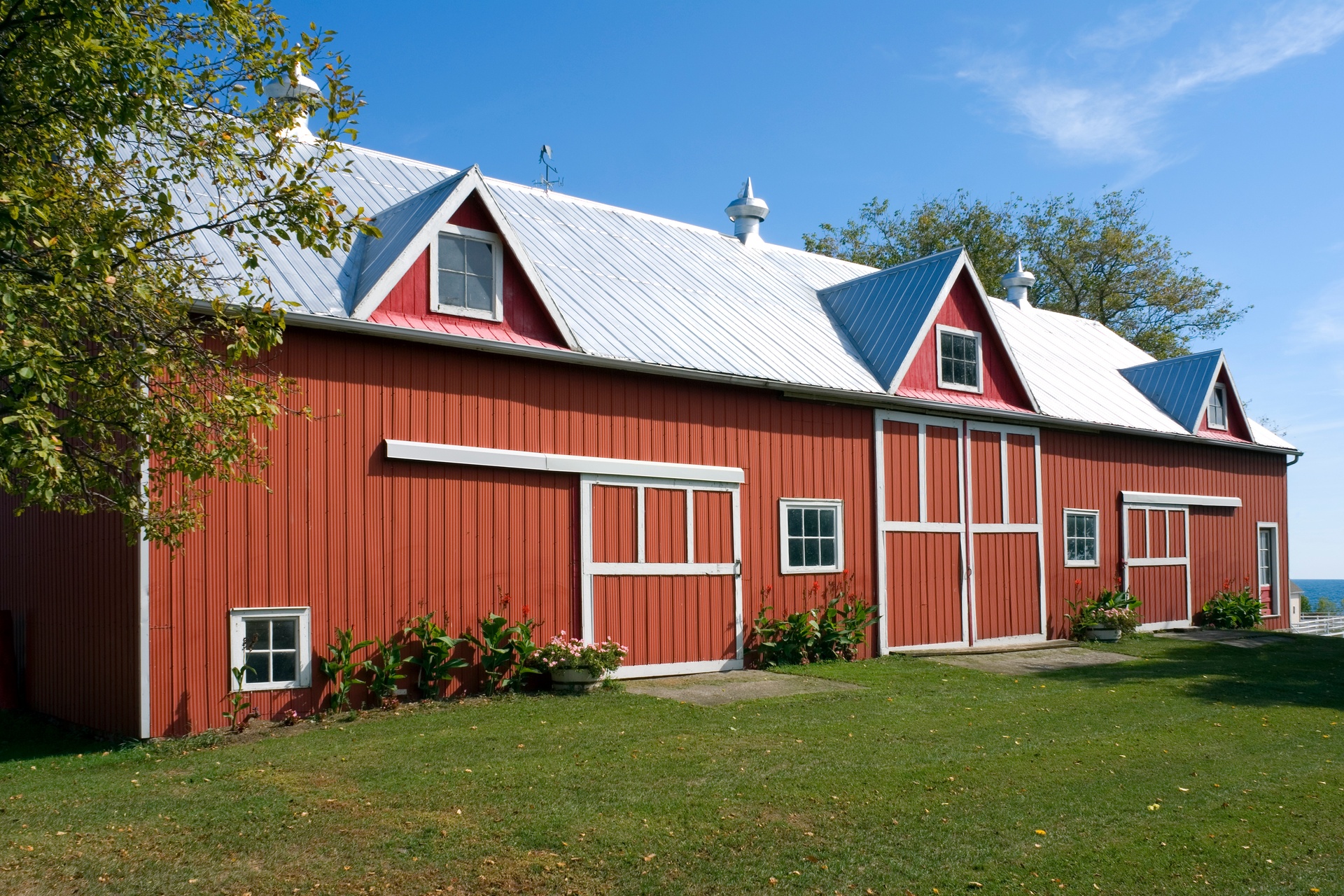 The exterior of a red steel barn with a silver roof and white accents surrounding the windows and doors.