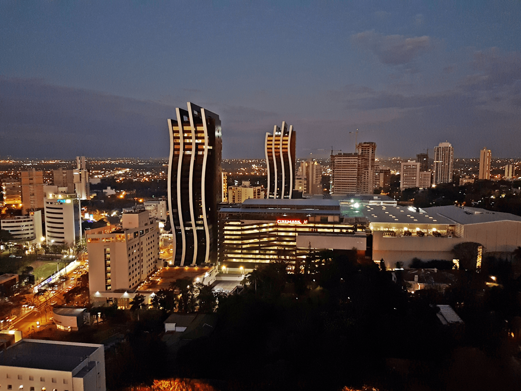 This image captures the modern skyline of Asunción, showcasing the city’s growing financial and commercial district at dusk. The iconic twin curved towers visible in the center are part of the Paseo La Galería complex, one of the most recognizable landmarks in the Paraguayan capital.
