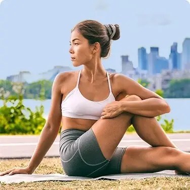 Young woman practicing yoga outdoors with city skyline in background.