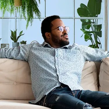 Man relaxing on a couch surrounded by plants.