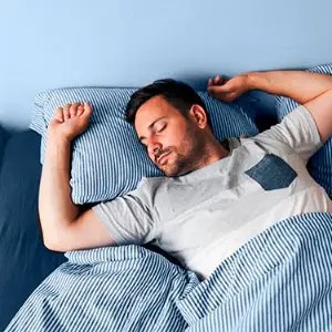 Man peacefully sleeping on a bed with blue bedding.