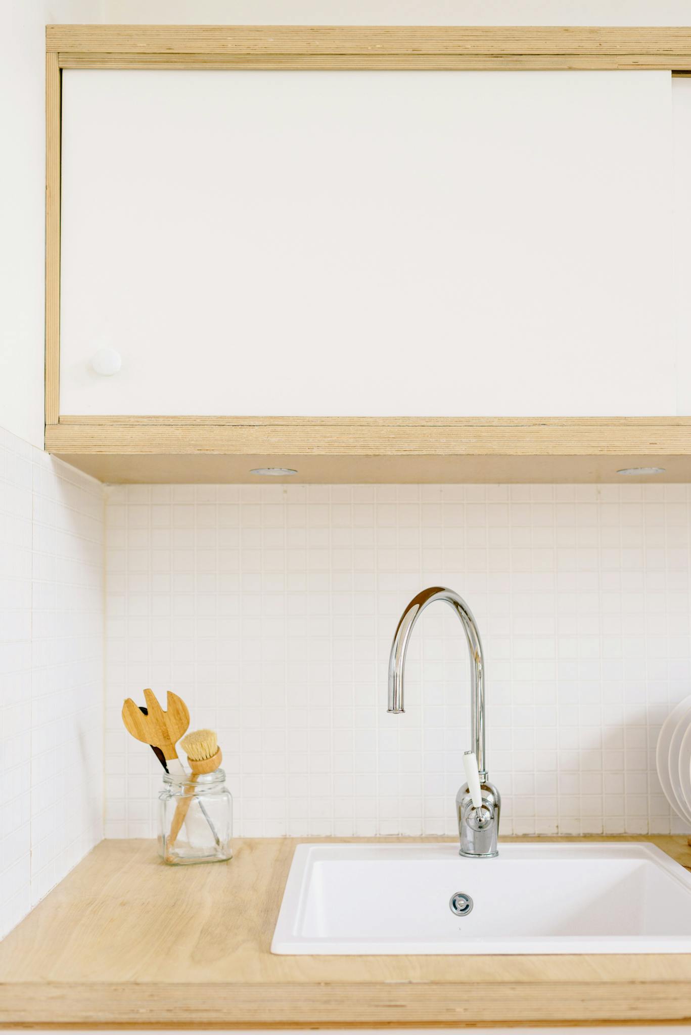 A clean, minimalist kitchen setup featuring a sink with wooden cabinets and modern fixtures.