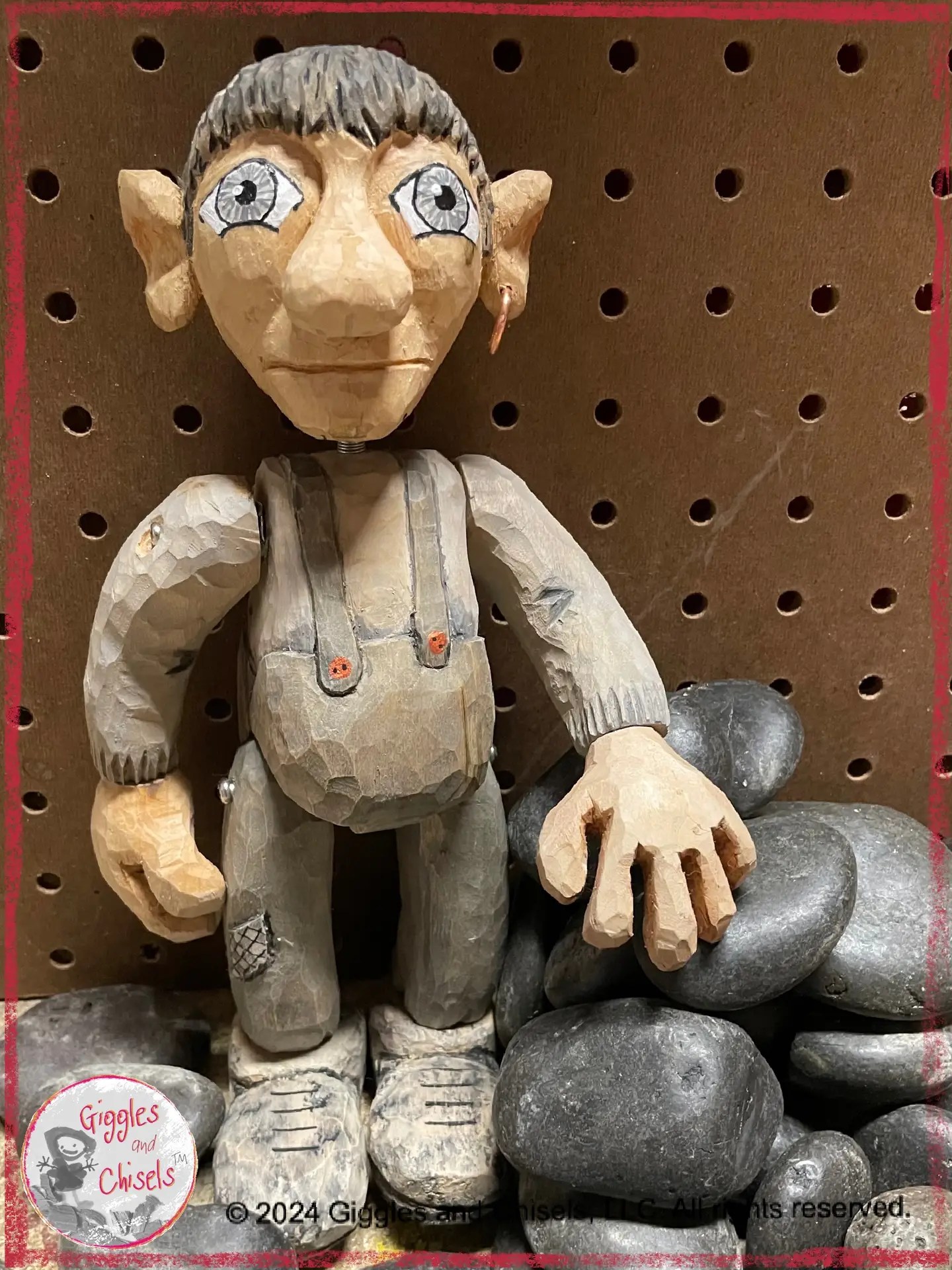 A wooden puppet, in grey shade, standing on a pile of black rounded rocks