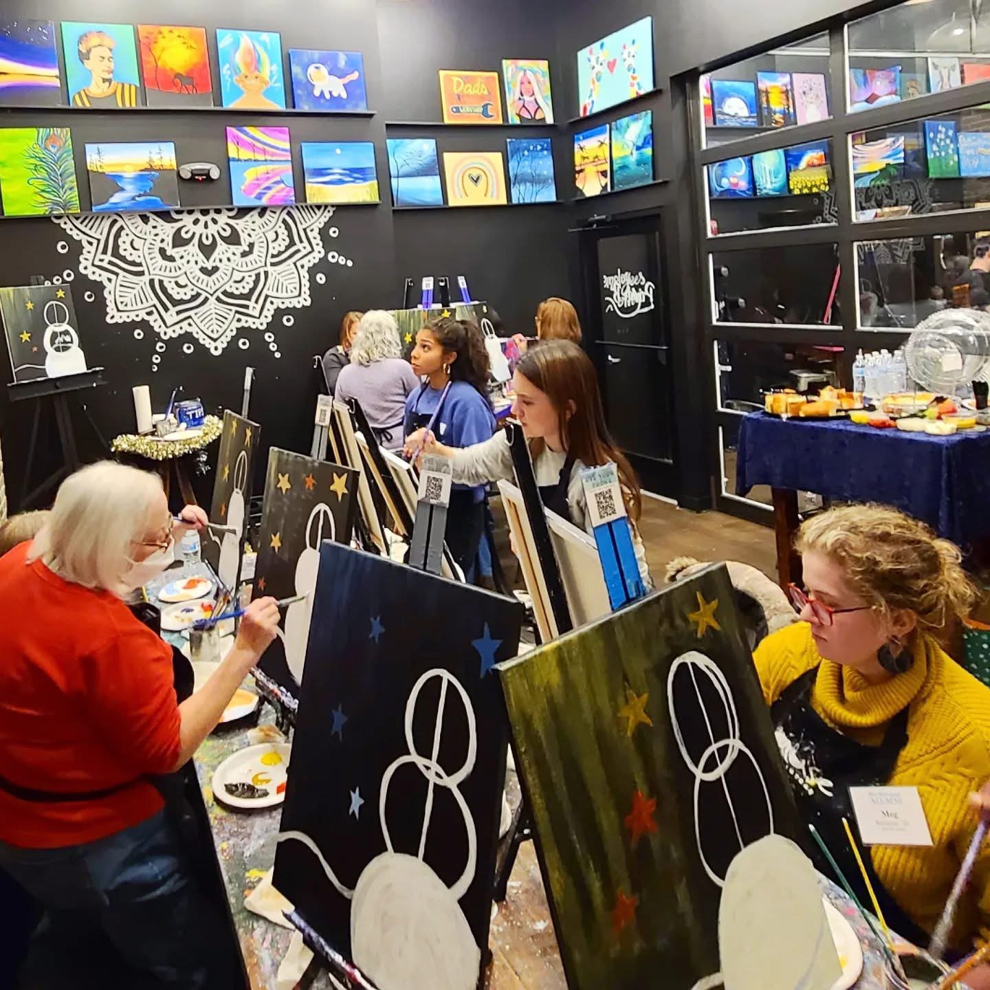A group of people paint snowmen in a paint bar.