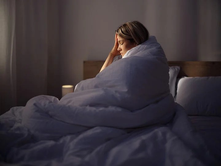 A woman who looks ashamed is propped up in bed.