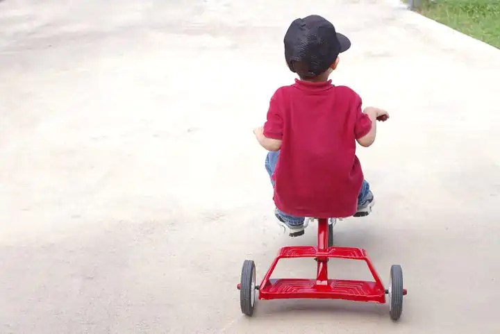 A young boy rides a tricyle on pavement.