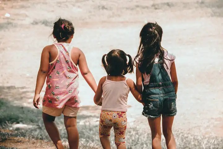 Three little girls walk along holding hands.