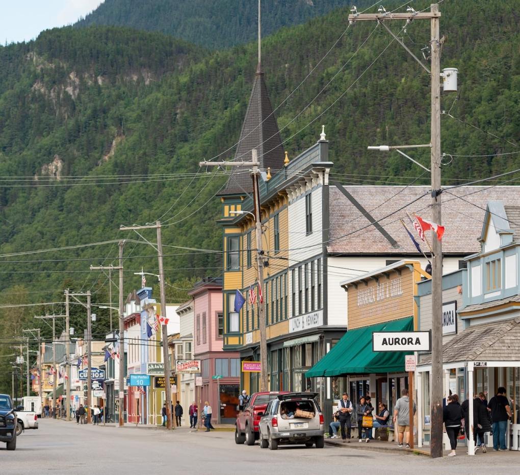 Historic downtown Skagway, Alaska, with colorful Gold Rush–era buildings and wooden boardwalks set against a backdrop of forested mountains, as visitors stroll along the street.