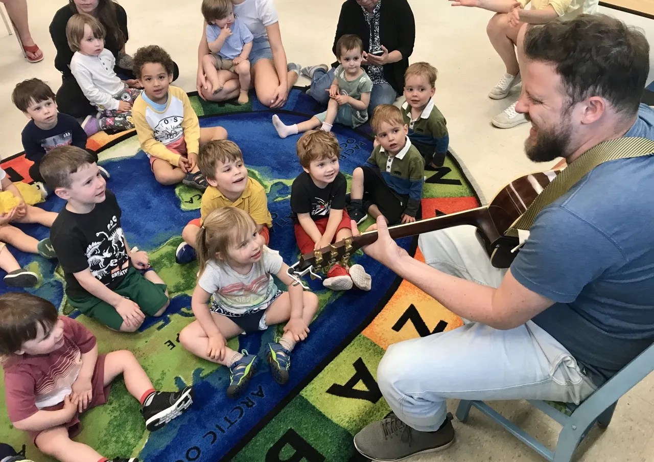 a photo of Jason Irvine leading a musical circle time and playing his guitar