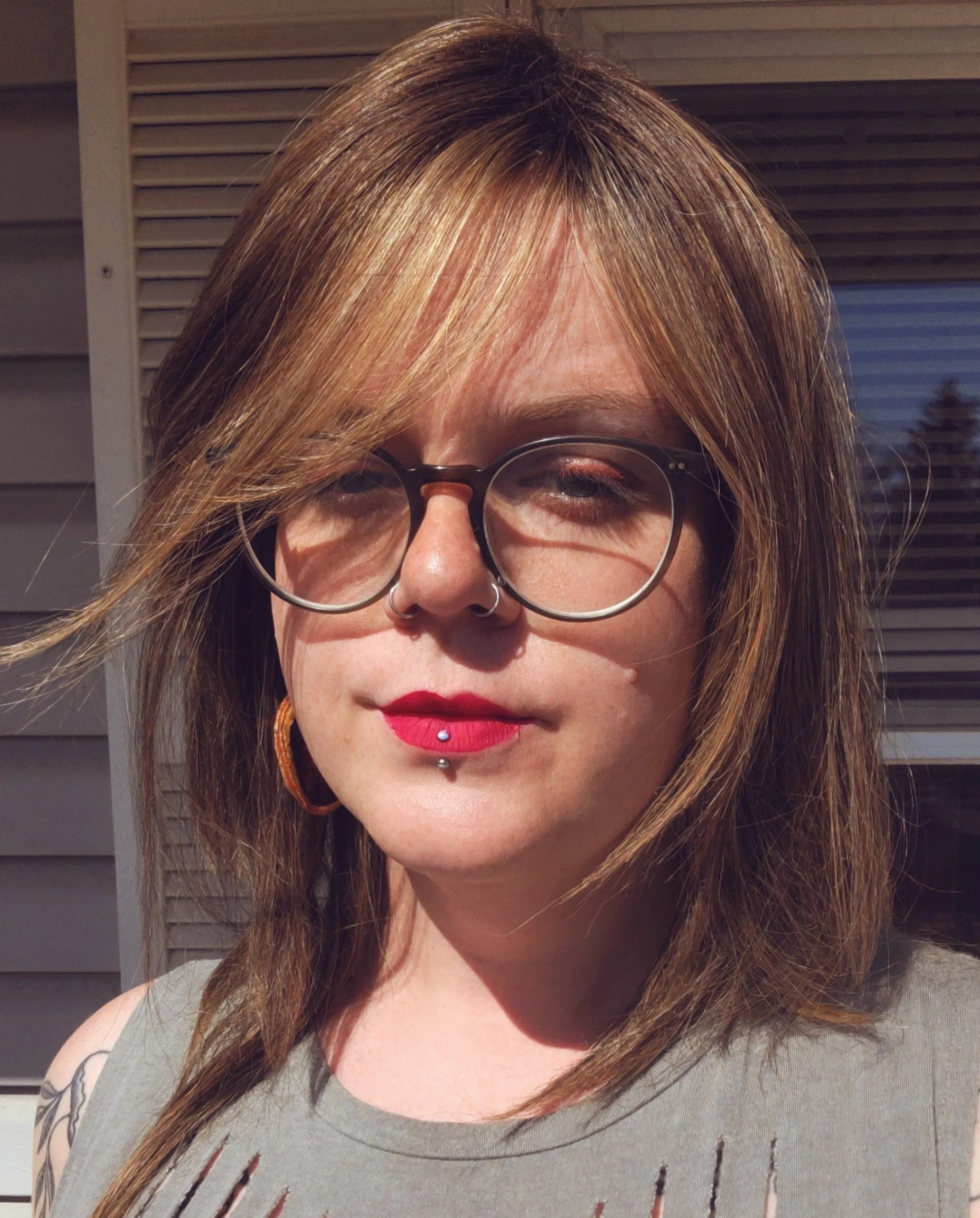 close up of woman wearing glasses with red listick and straight blond hair with a grey shirt
