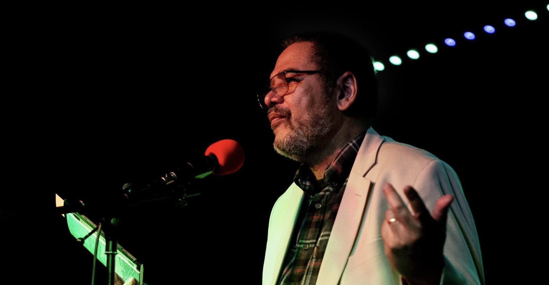 a man wearing glasses and a white jacket in front of a microphone