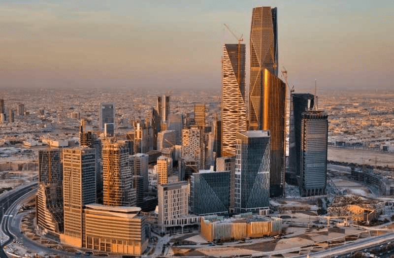 منظر جوي لأفق مدينة حديثة يضم أبراجًا شاهقة ومعمارًا معاصرًا وشبكة طرق رئيسية عند الغروب.