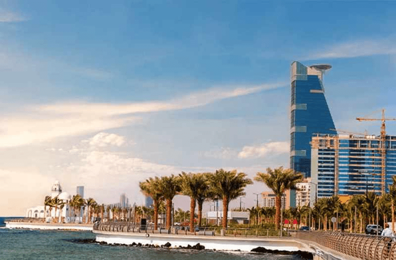 ممشى ساحلي يضم أشجار نخيل ومبانٍ حديثة مطلة على البحر وأفقًا حضريًا معاصرًا.