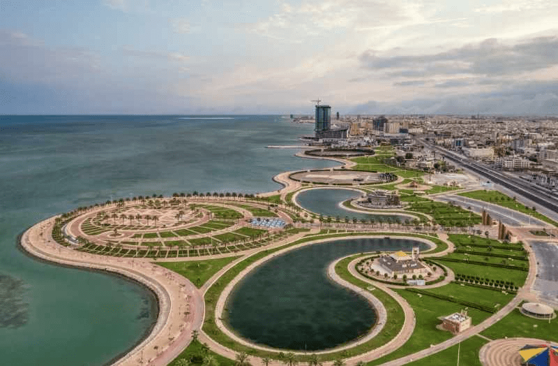 منظر جوي لمدينة ساحلية تضم حدائق واجهات بحرية ومسارات منحنية وبحيرات صناعية وأفقًا حضريًا.