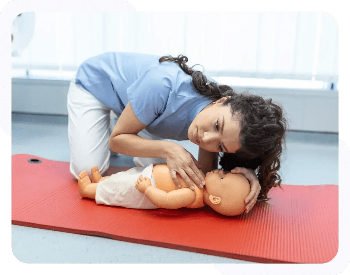 A person performing CPR on an infant manikin on a red mat in a training environment.