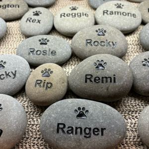 Multiple pet stones are shown with engraved paw prints and engraved pet names.