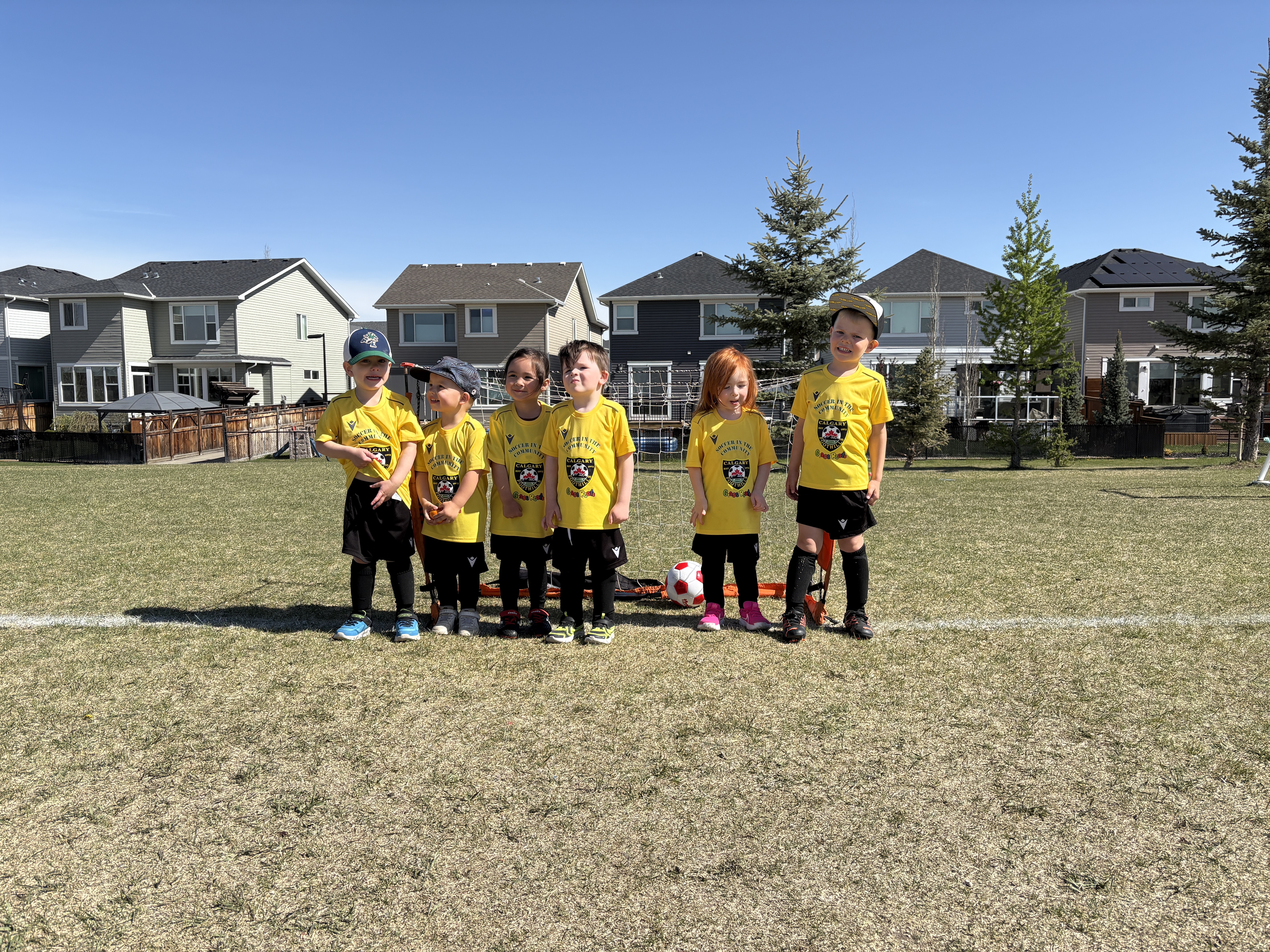 Calgary Foothills Soccer Club grassroots players (U4–U8) standing in a row on the field wearing yellow jerseys during a sunny outdoor soccer session.