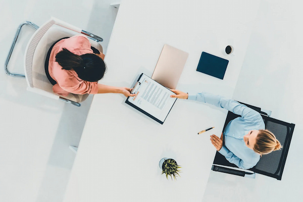 two-young-women-meeting-on-a-job-interview-while-one-of-them-hands-their-employee-data-management-policy-to-the-other-one