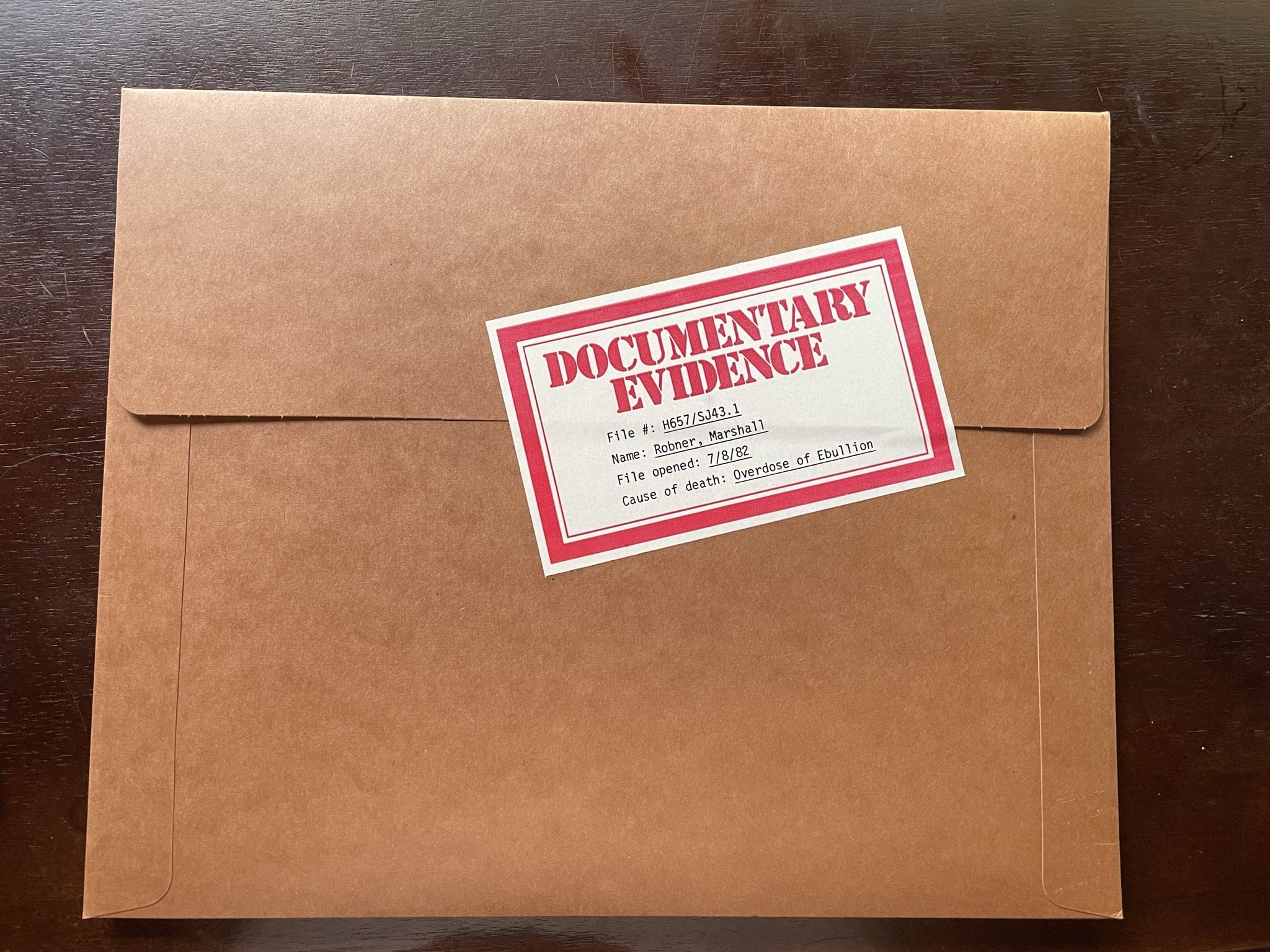 The sealed crime dossier included with Deadline. A brown folder sealed with a red and white "DOCUMENTARY EVIDENCE" label.