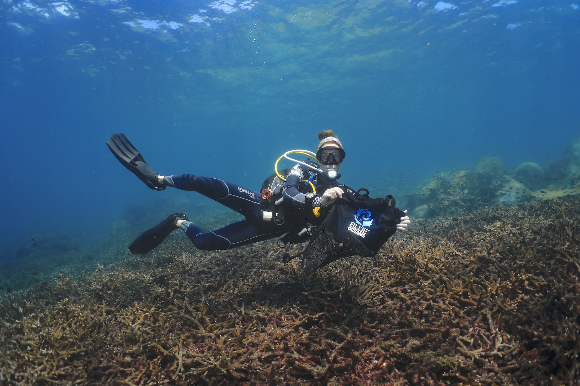 Diver engaged in ocean conservation, holding a bag above coral reef, promoting marine environment protection.
