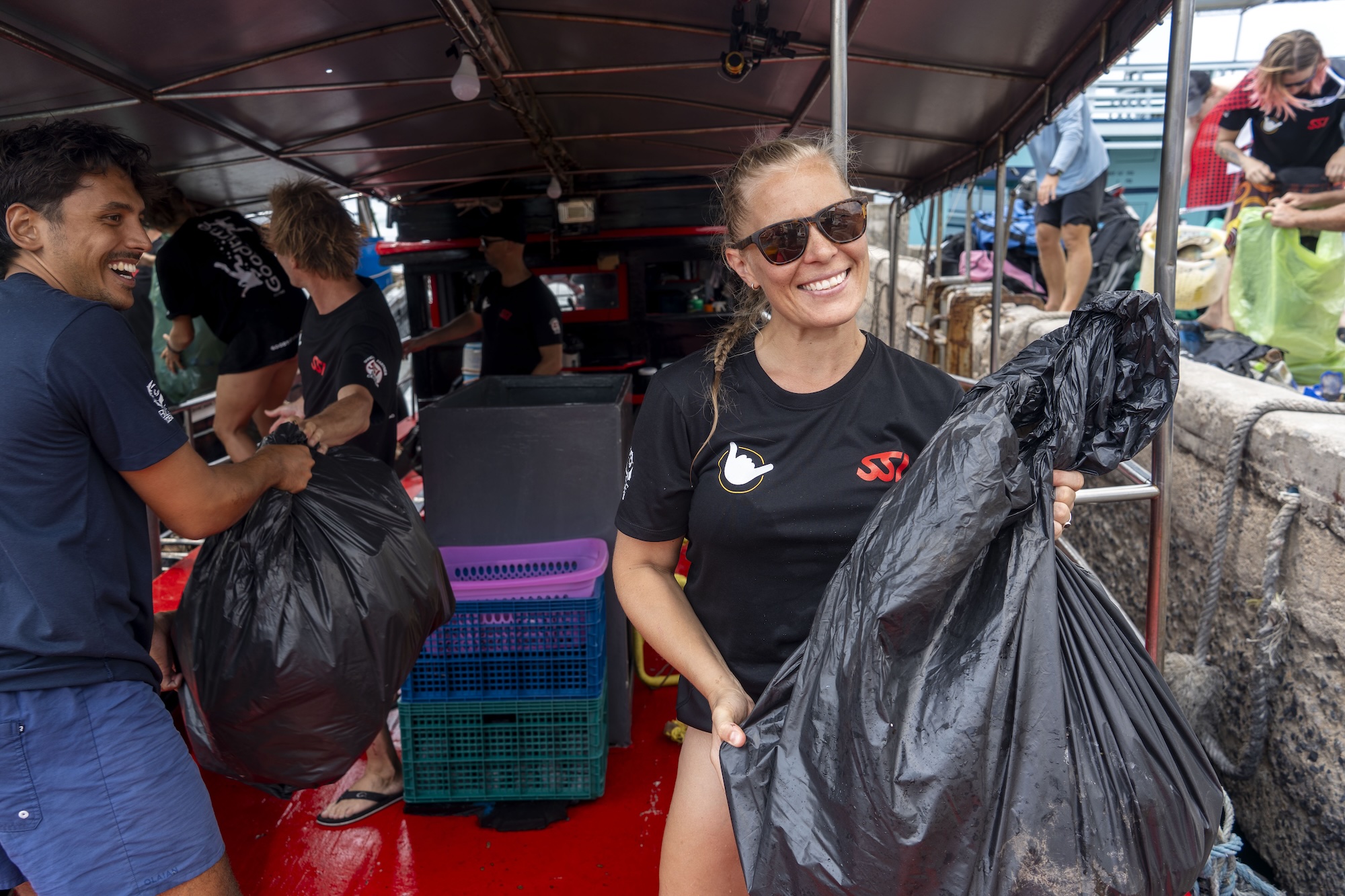 Volunteers smiling and holding bags during a community cleanup on a boat.
