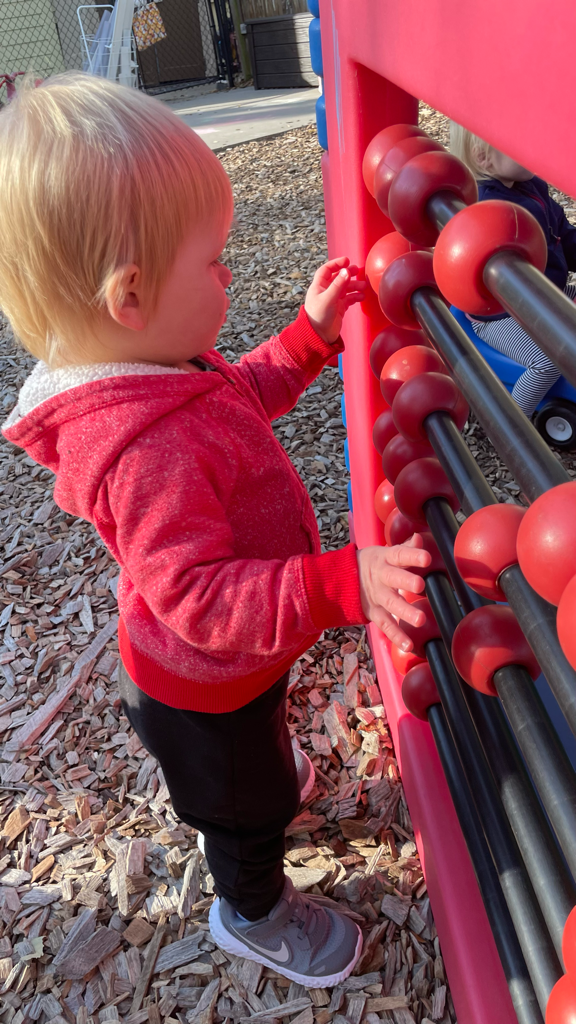 toddler with red zip sweatshirt inspecting large red abacus