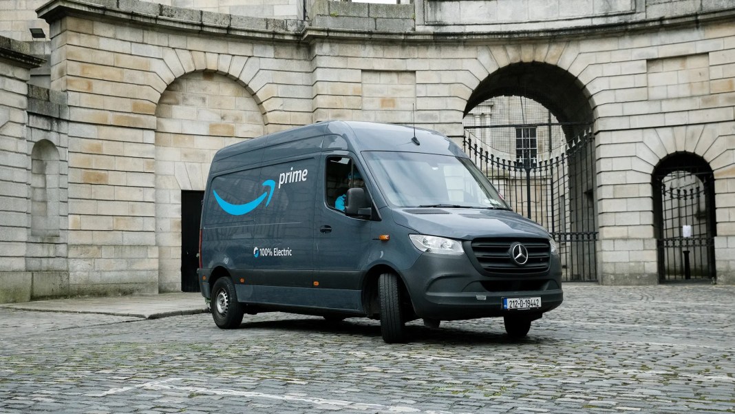 Amazon Prime 100% electric delivery van parked in front of a historic stone building with arched doorways.