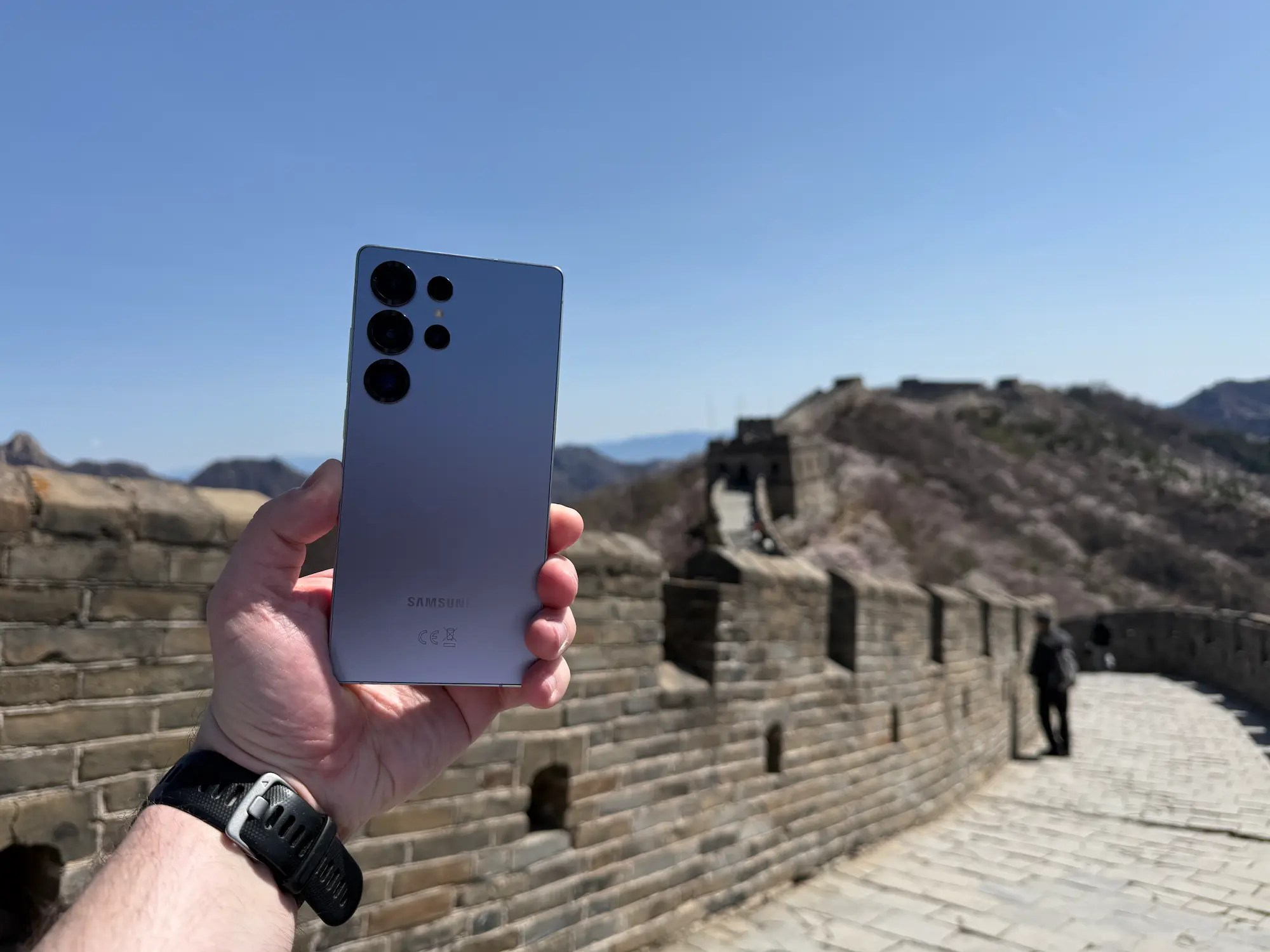 Person holding a Samsung Galaxy S25 Ultra on the Great Wall of China under a clear blue sky.