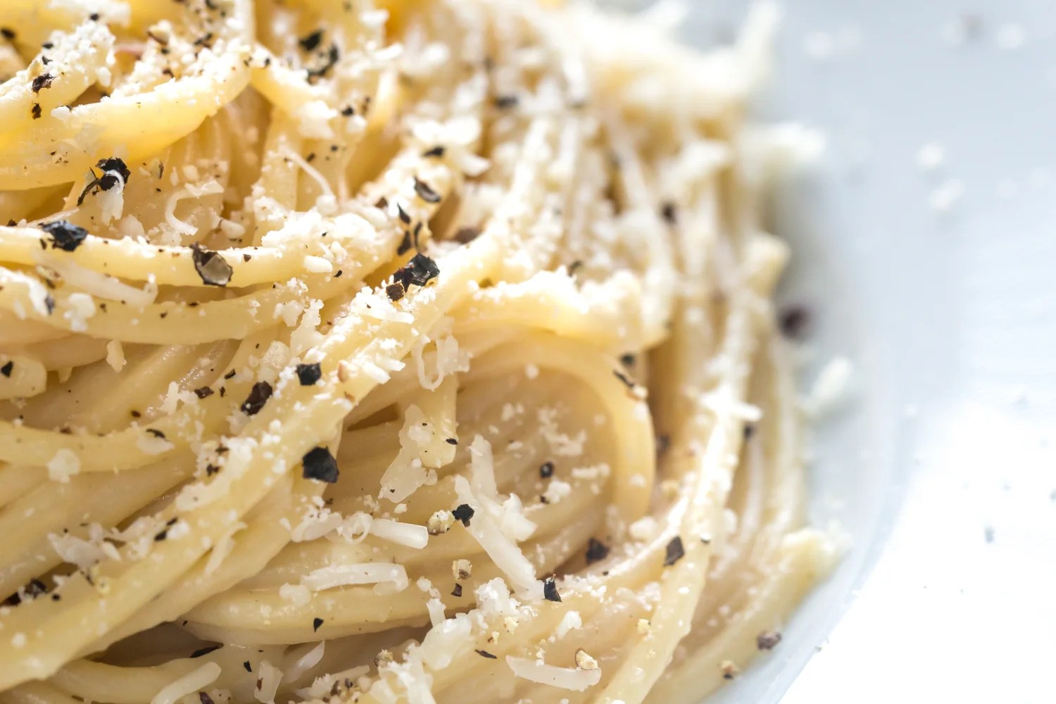 A bowl of authentic cacio e pepe with long pasta strands coated in a creamy emulsified Pecorino Romano and black pepper sauce, finished with extra grated cheese