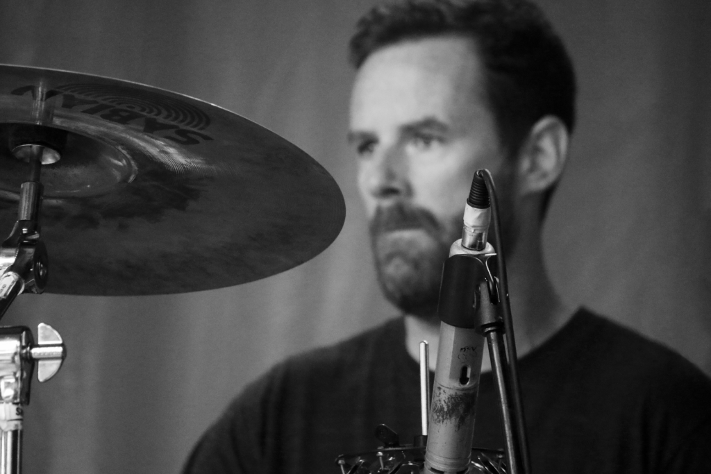 Black and white photo showing a slightly blurred Peter Lemon, the drummer for BC band The Matinee, sitting at his station.