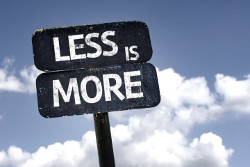 Sign saying "Less Is More" against blue sky with clouds