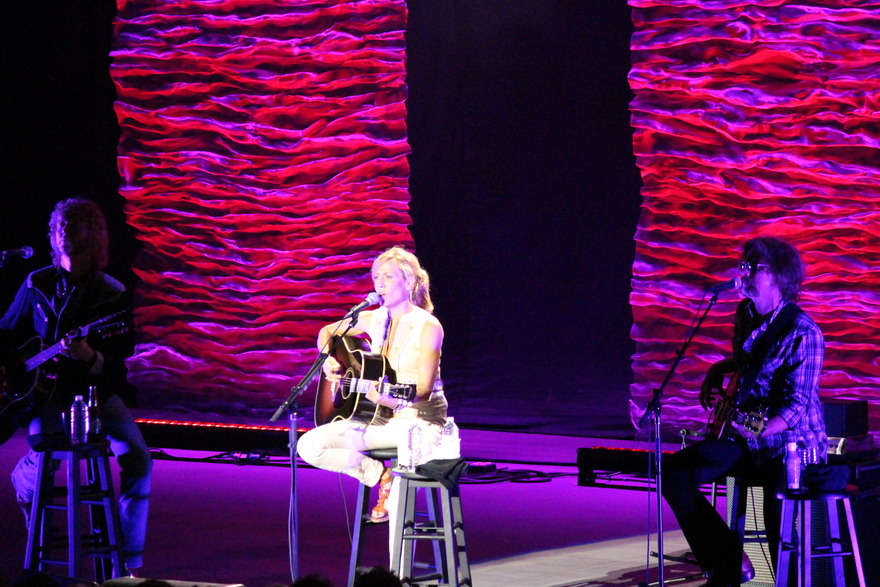 Three musicians seated against a pink backdrop