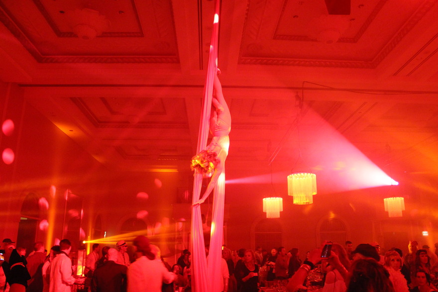 Aerial silk performer in a red-lit ballroom